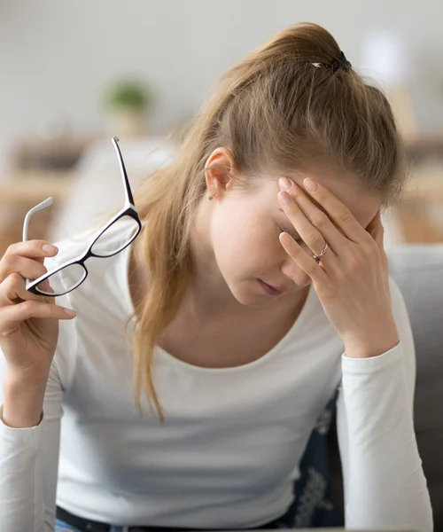 A woman taking off her eyeglasses and holding her head in pain